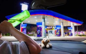 A man drink and driving as he pulls into a gas station.